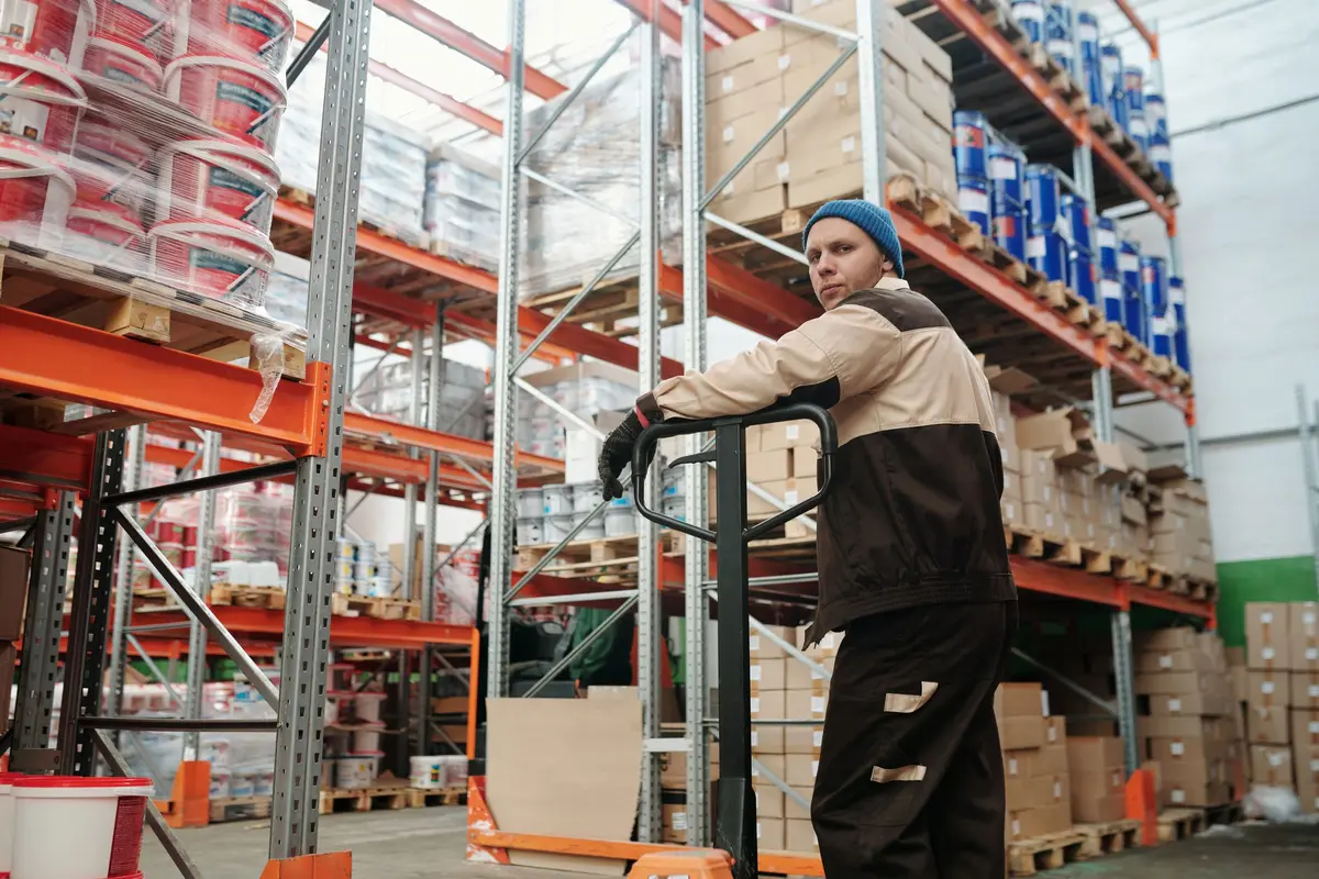 Warehouse operative moving goods on a pallet truck between racking